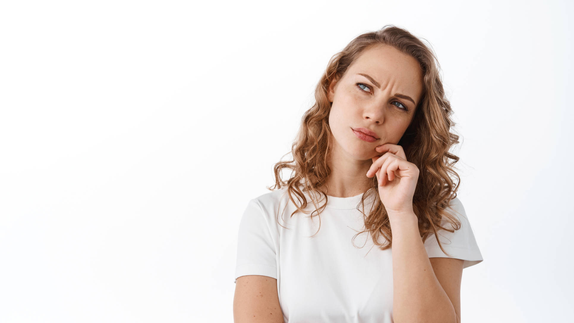 Thoughtful blond woman pondering, frowning and looking puzzled at upper left corner promo text, thinking, making decision, standing over white background.